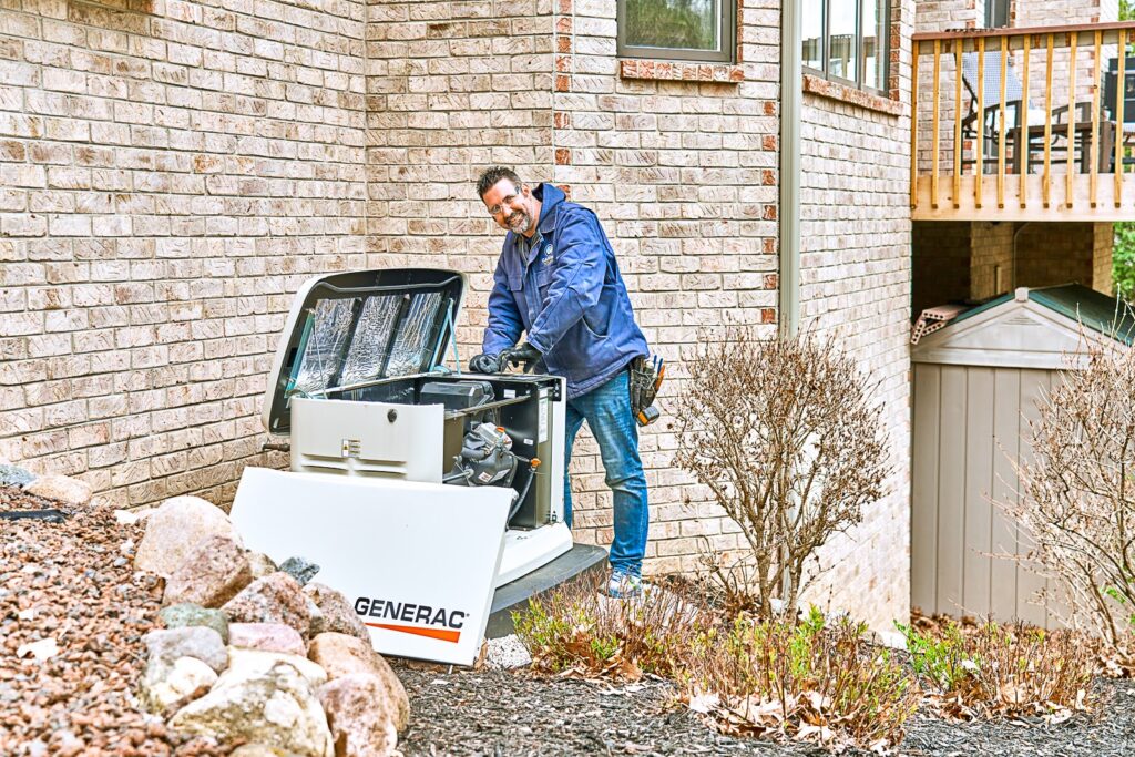 A man in a blue jacket expertly repairs a Generac generator beside a brick house, using Milwaukee tools to guarantee smooth and cool operation.